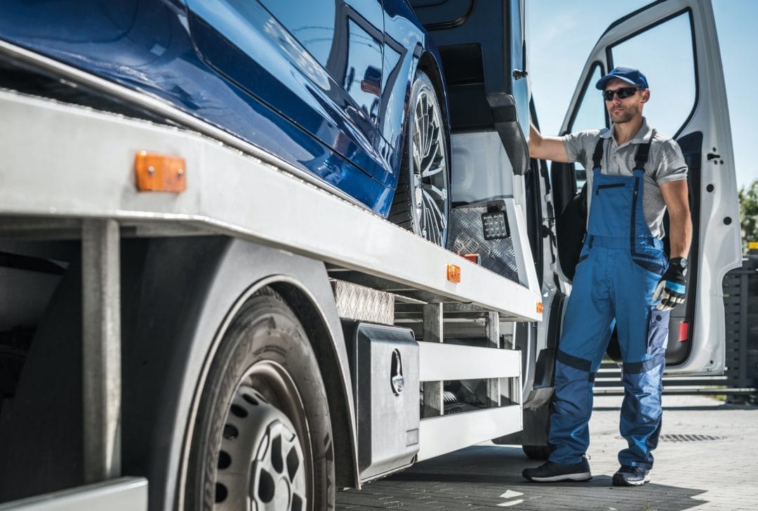 Towing professional securing a blue vehicle on a flatbed tow truck